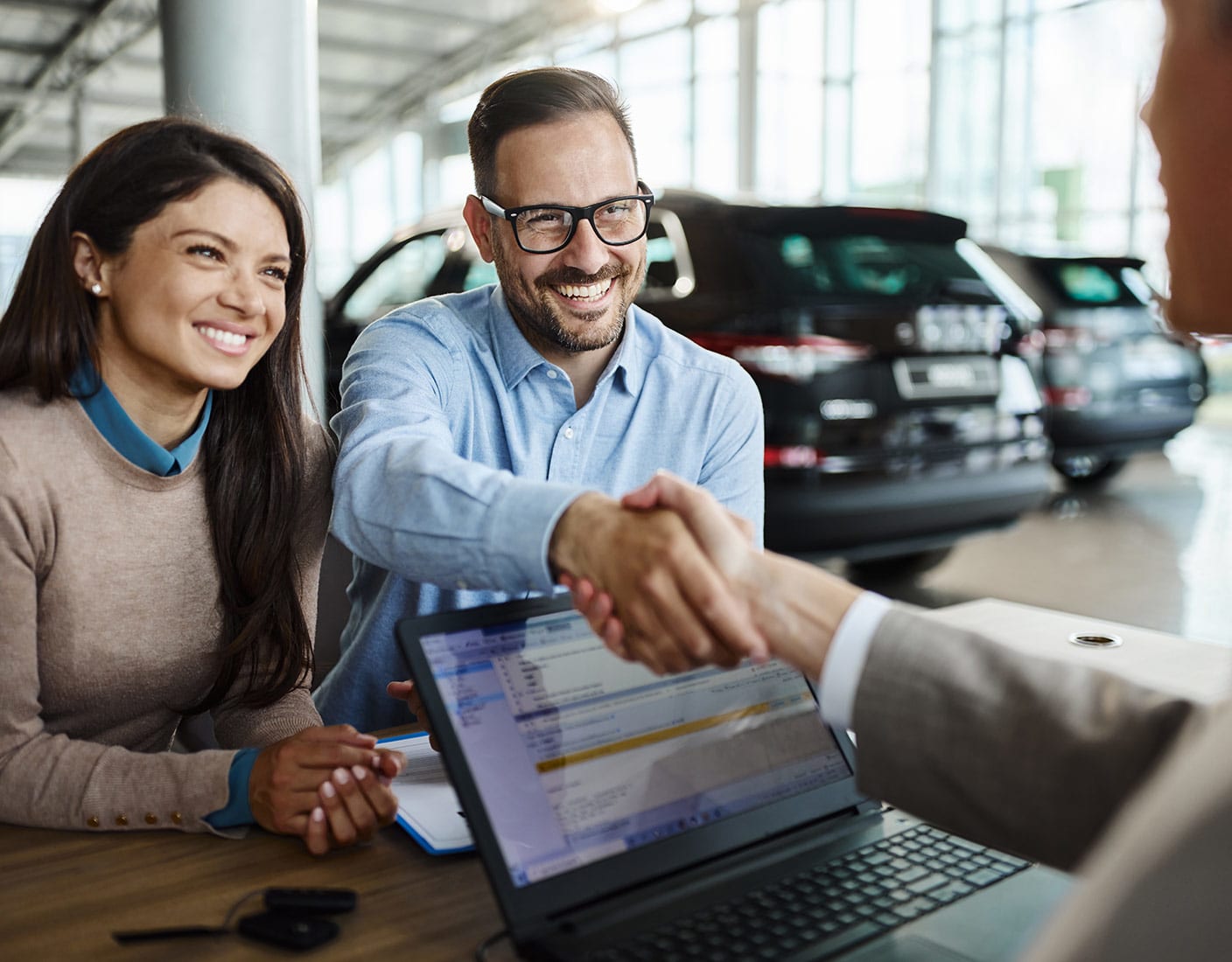 A man and woman shaking hands inside a car dealership, representing a business agreement or sale.